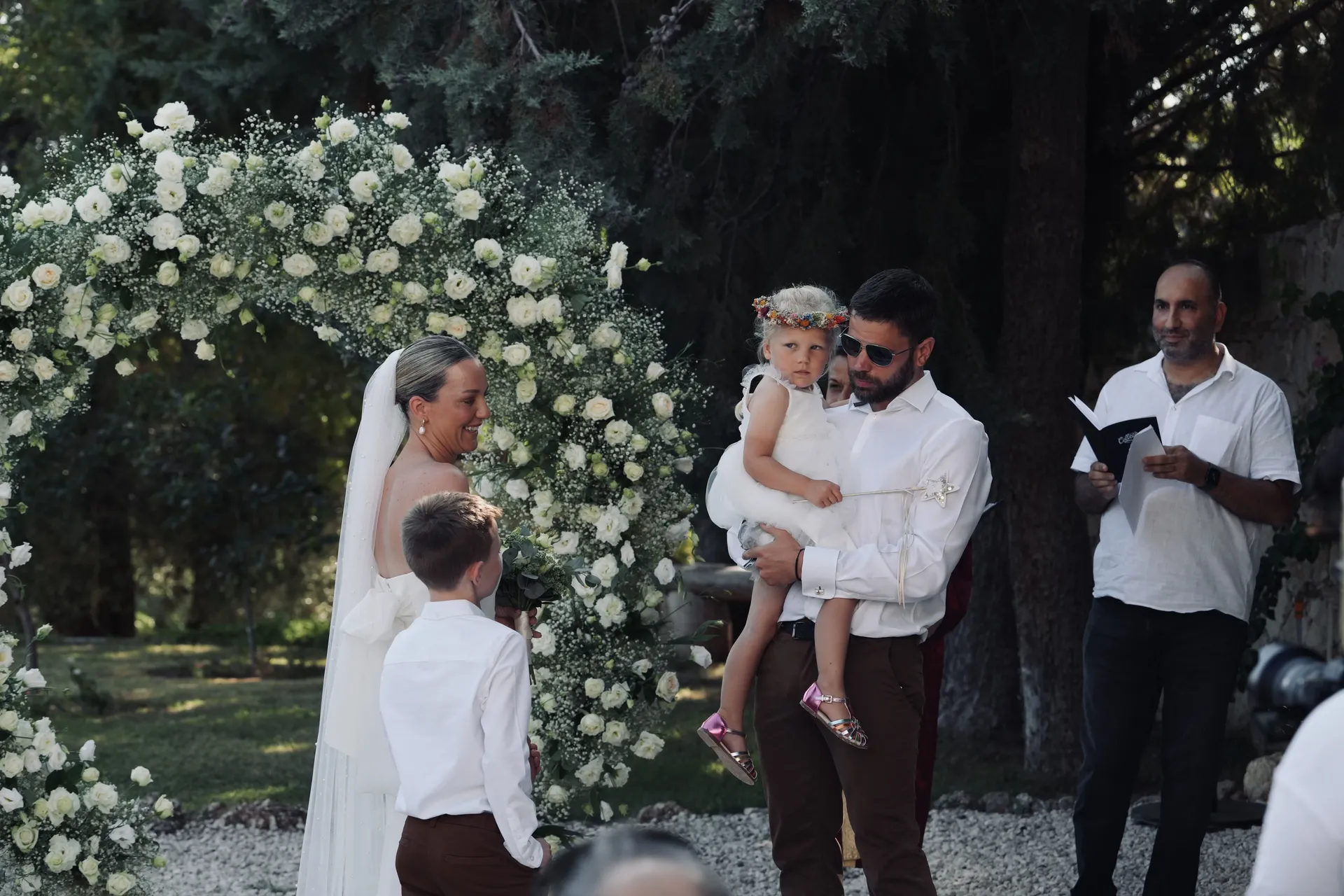 Wedding ceremony with toddler under white rose floral arch