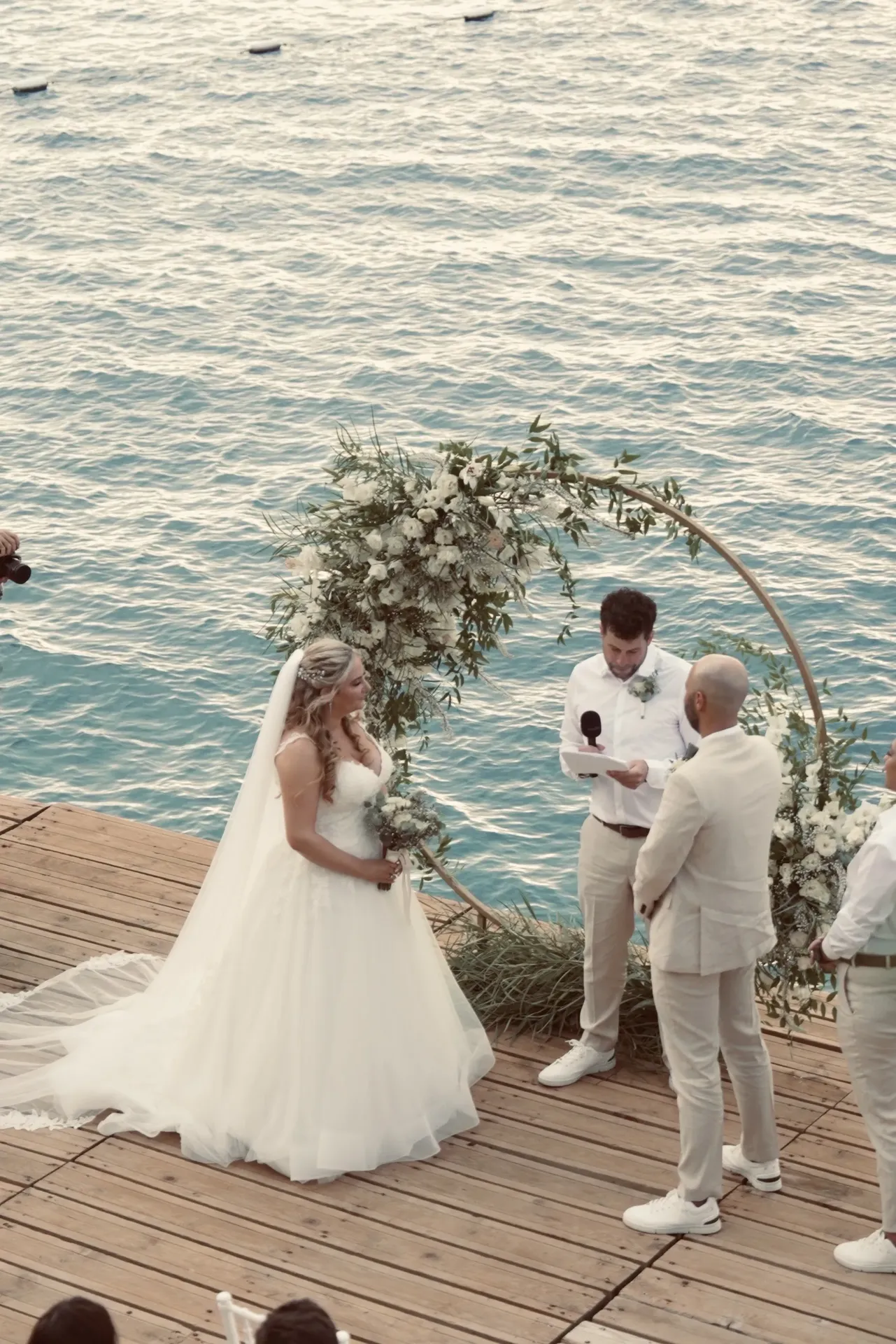 Wedding ceremony on wooden deck platform over turquoise Mediterranean water