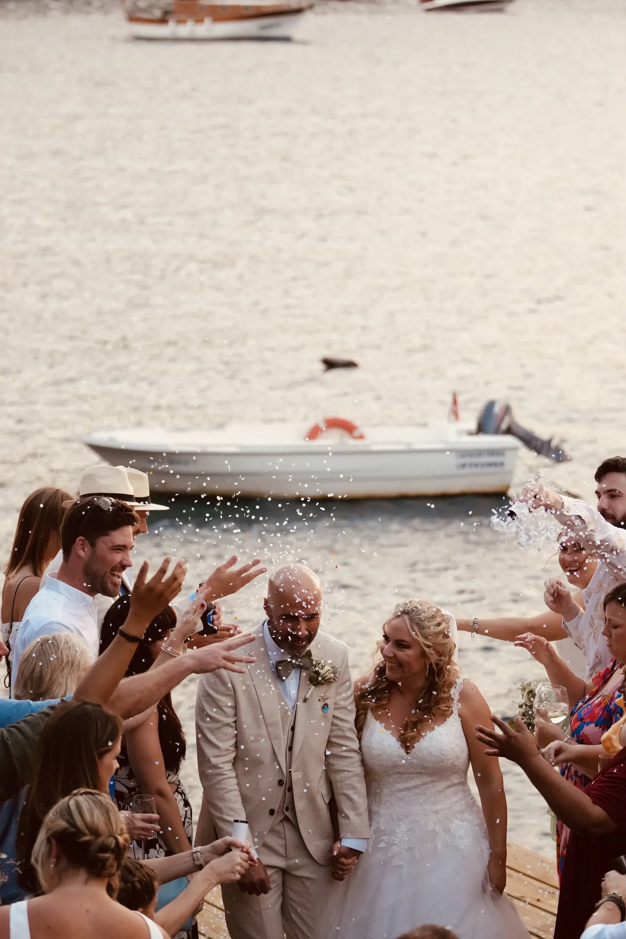 Couple showered with confetti at beach ceremony with boat in background
