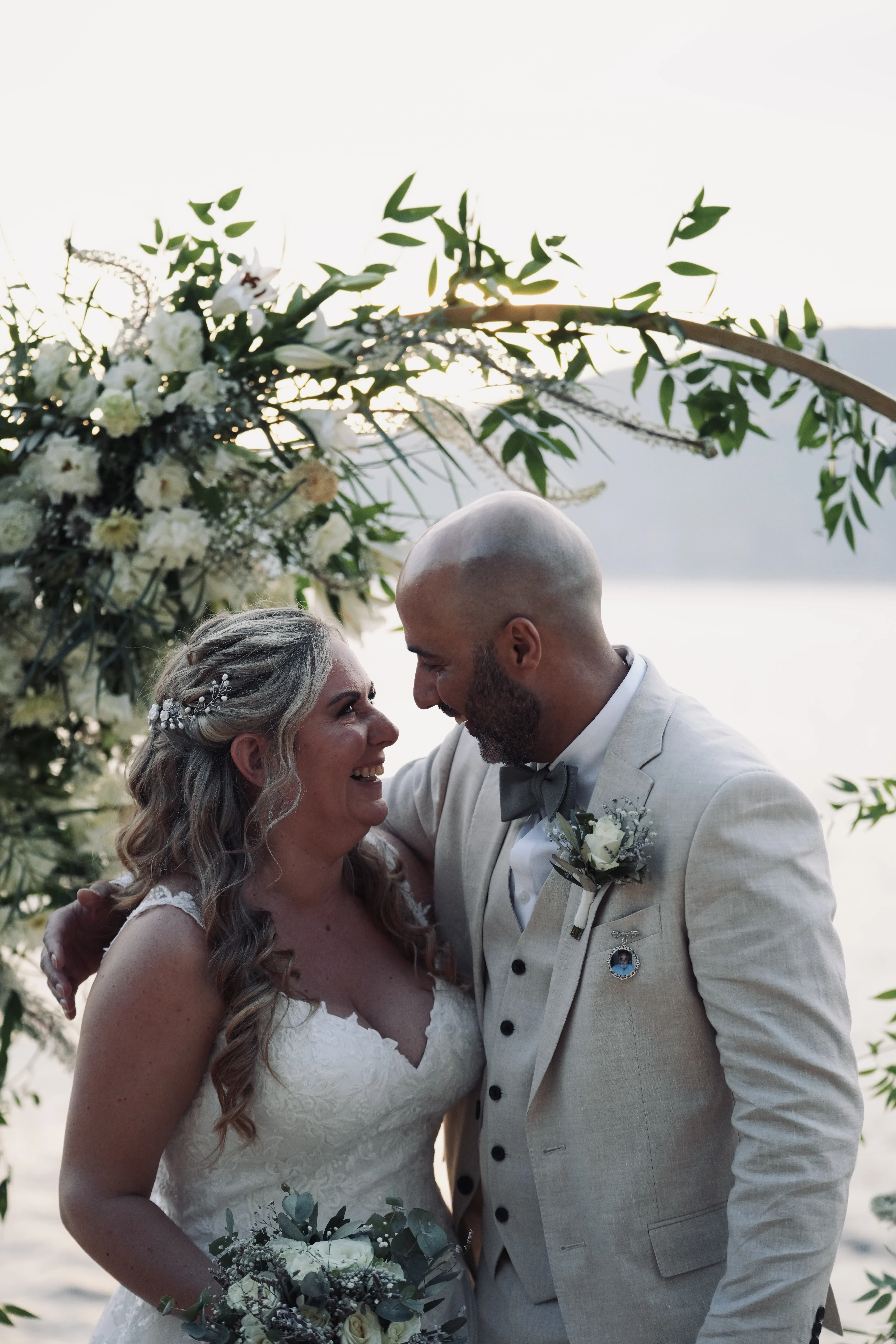 Newlyweds standing under curved white floral arch